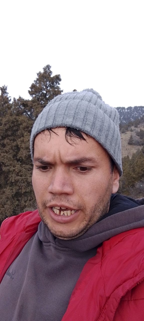 Мужчина на прогулке в красной куртке и серой шапке делает странное лицо.