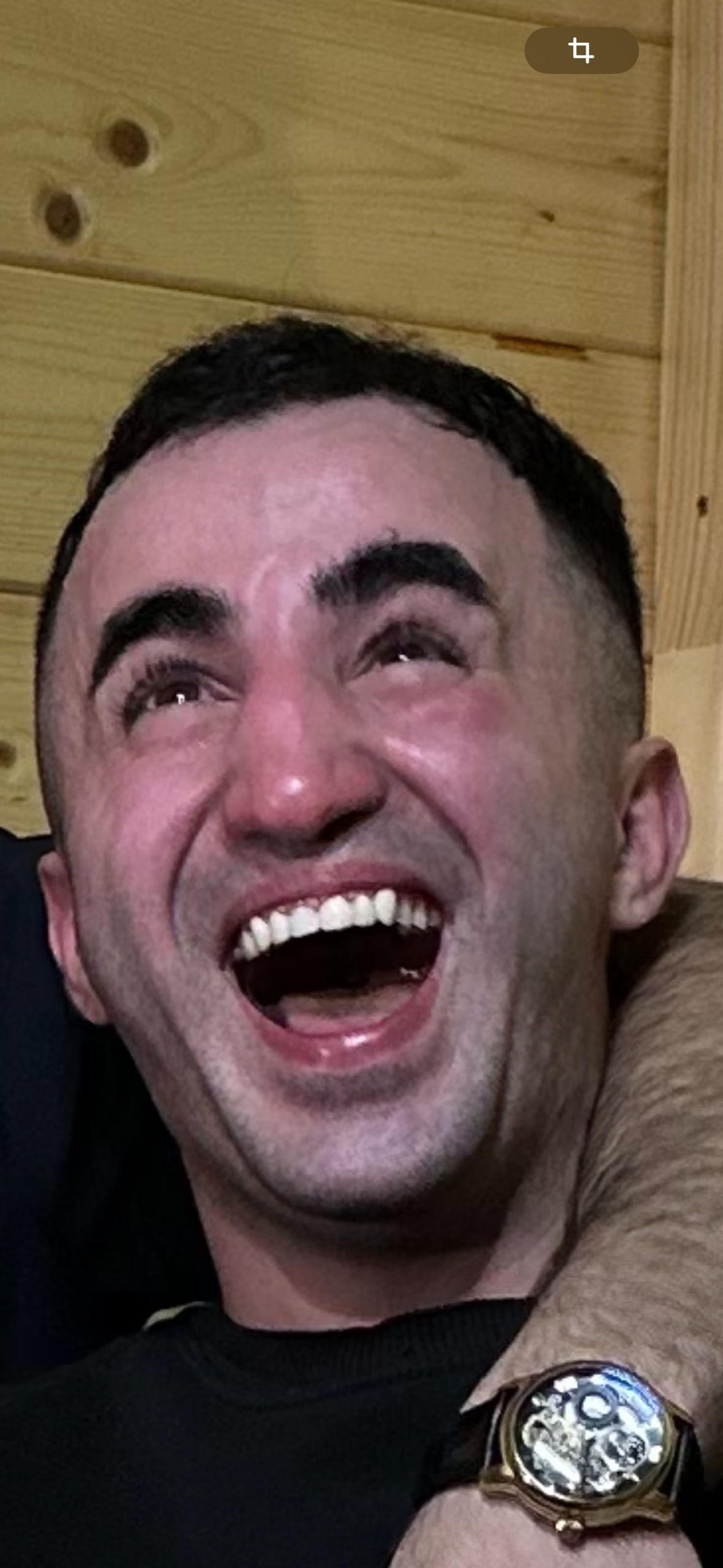 Мужчина смеётся в кадре, на фоне деревянной стены, рука друга рядом.