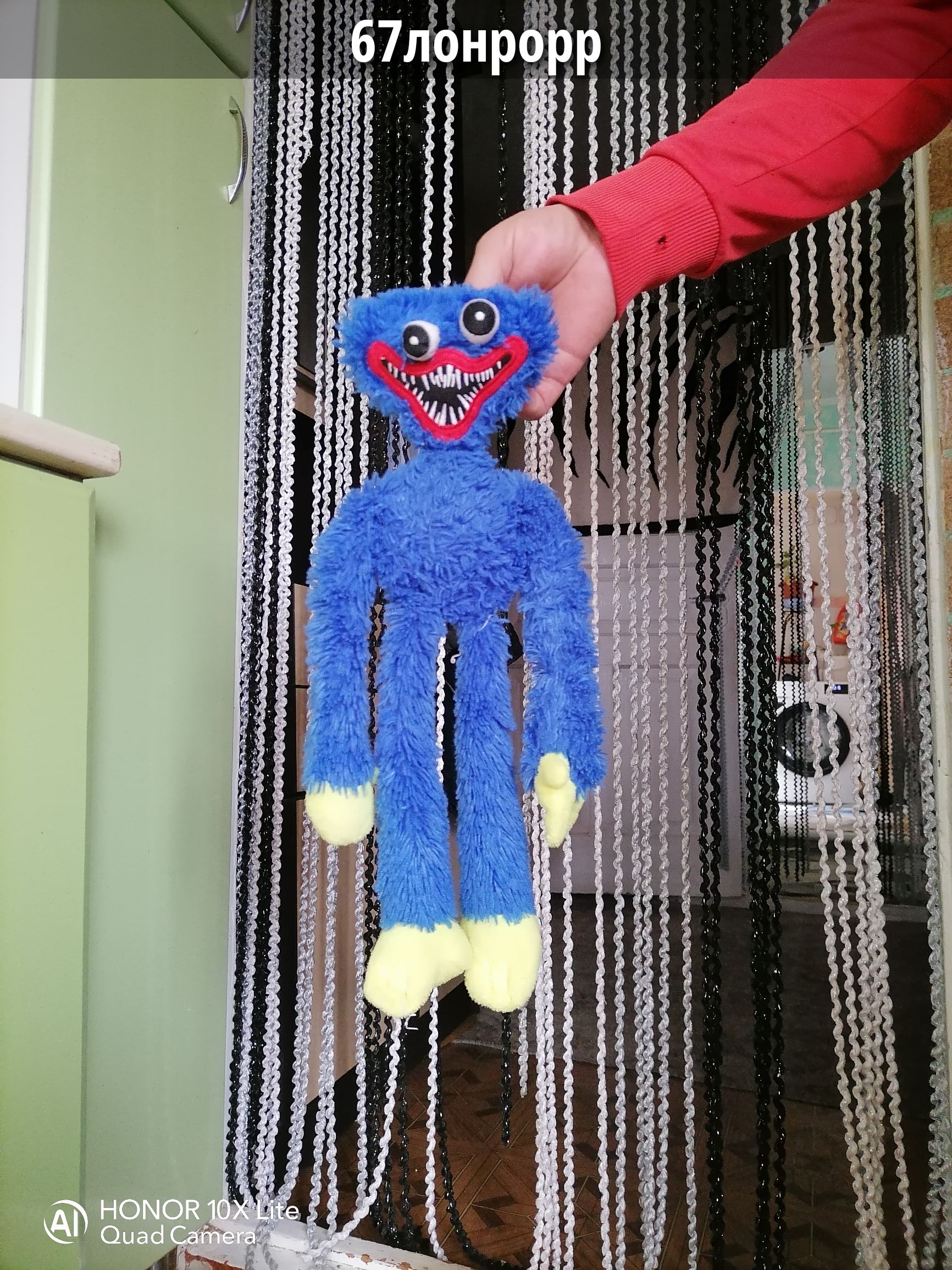 67лонрорр. HONOR 10X Lite Quad Camera. Рука держит синюю плюшевую игрушку Хагги Вагги с красным ртом и острыми зубами.