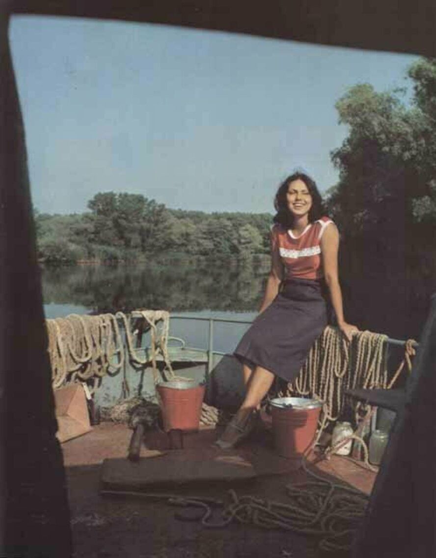 Женщина сидит на борту лодки у причала, вокруг канаты и ведро