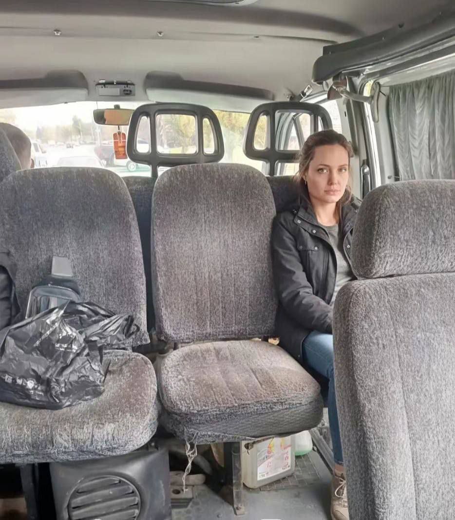 Женщина сидит в салоне микроавтобуса рядом с мешком и пустыми сиденьями.