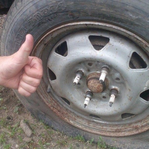 Ржавое колесо автомобиля с шестью шпильками и пустым центральным ступичным узлом, рядом рука с большим пальцем вверх.