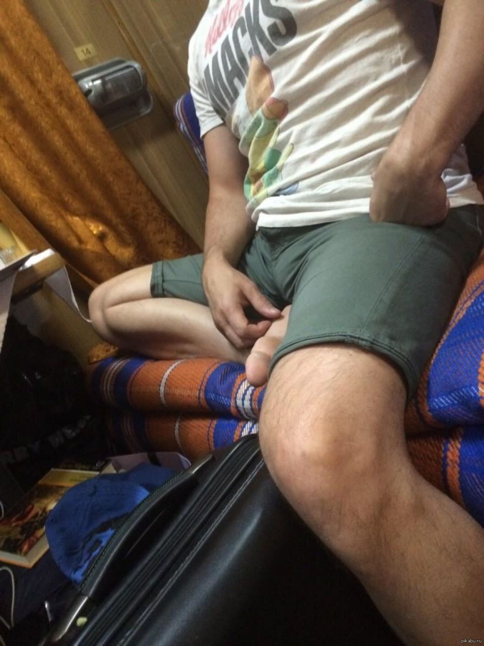 Мужчина в шортах сидит на диване, руки возле паховой области.