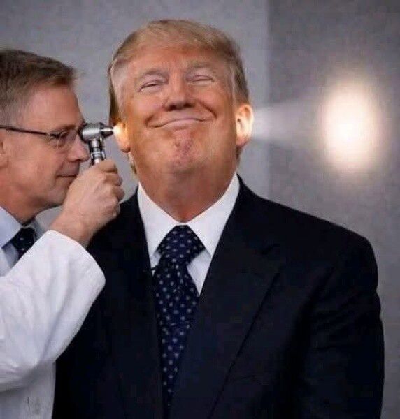 Человек в костюме улыбается, врач осматривает его ухо зондом