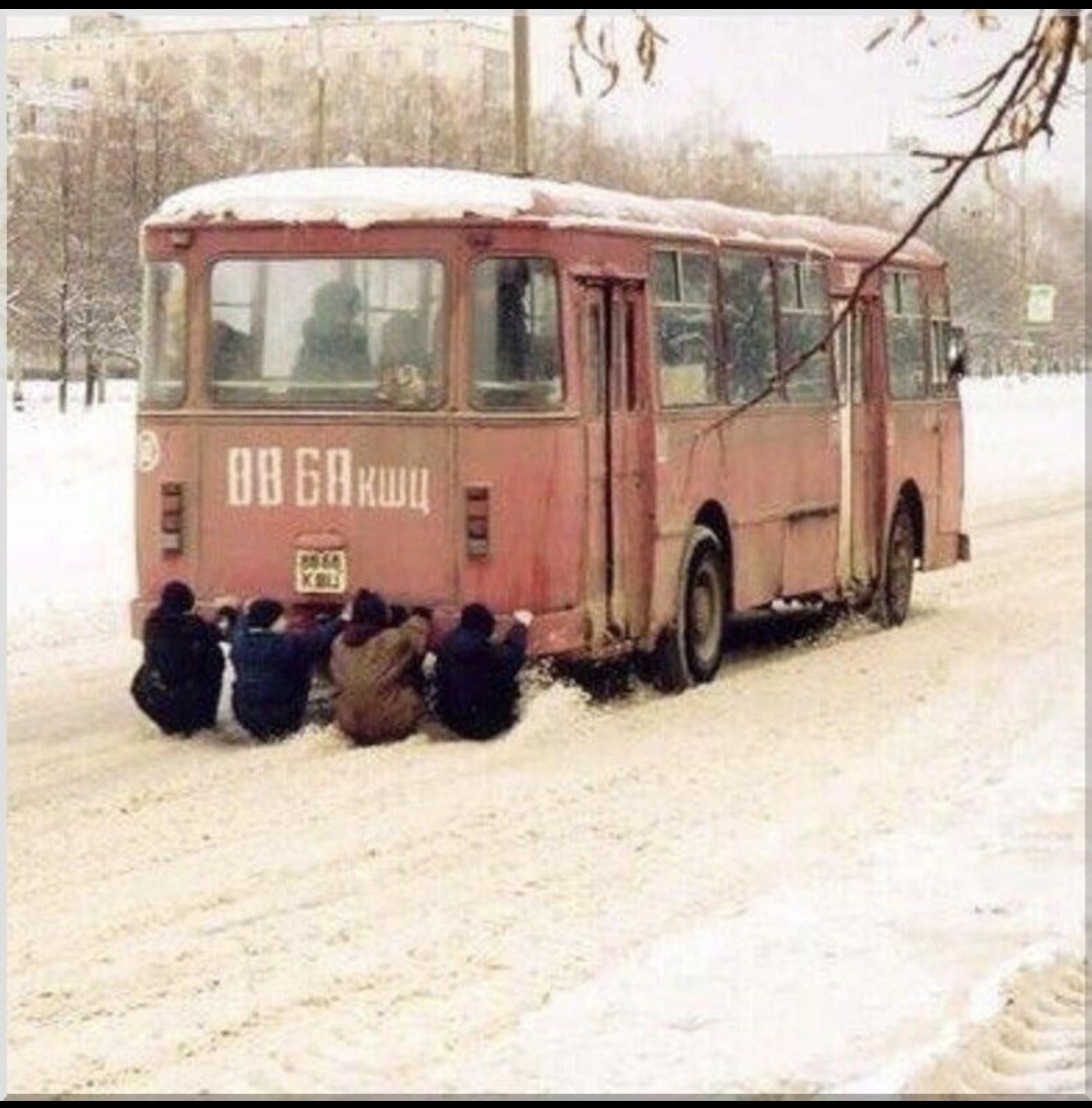 Старый автобус застрял в снегу, рядом сидят группа детей.