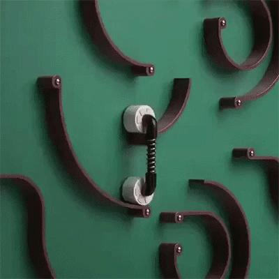 Зелёная стена с абстрактной скульптурой из дуг и центральной деталью, напоминающей телефонную трубку, соединённой с двумя белыми зажимами.