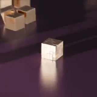 Маленький блестящий куб на фиолетовой поверхности, в фоне видны коробки.