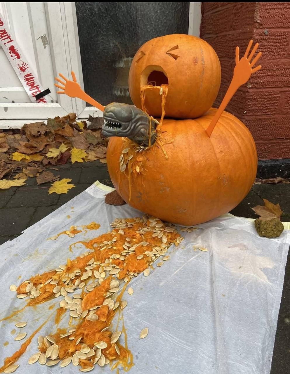 Забавная Halloween-инсталляция: две тыквы, одна на другой, с бумаженными руками, клыками и посыпанные семечки.