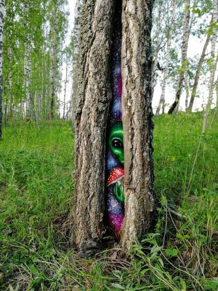 Дерево с расколотой корой, в щели прячется яркий рисунок с инопланетянином и грибом.