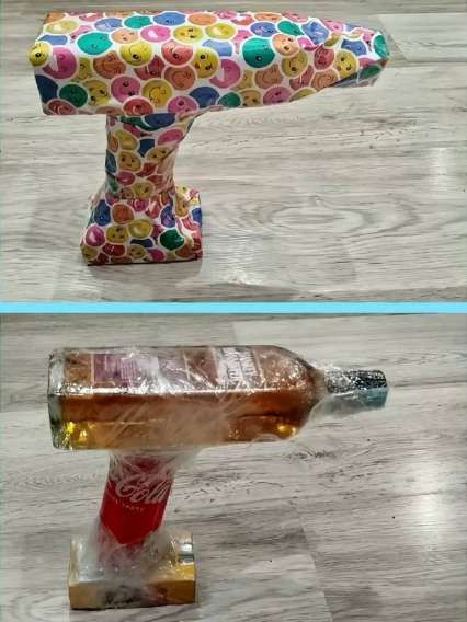 На столе стоит выкрашенная игрушечная пушка, обклеенная смайликами, под ней — бутылка Coca-Cola на подставке.