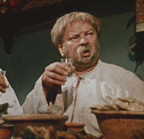 Старая комедия: мужчина поднимает бокал за столом на пиршстве.