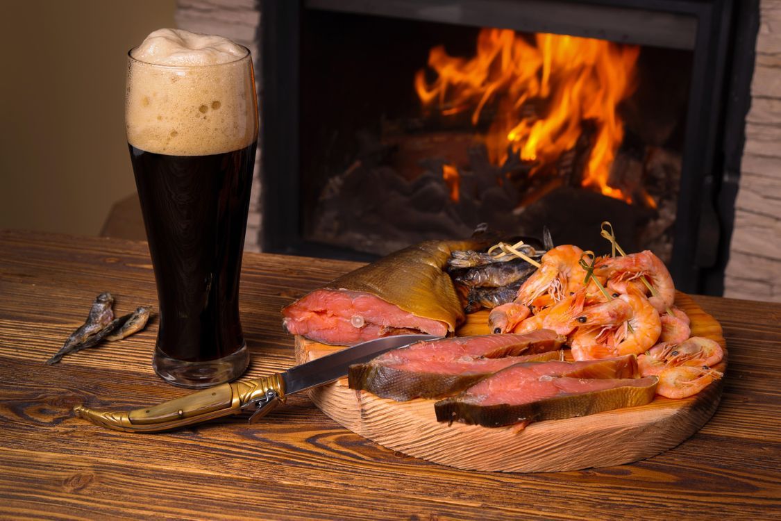 Стейк и морепродукты на деревянной доске у камина с бокалом пива