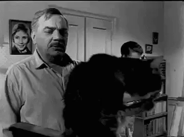 Чёрно‑белое фото мужчины, держащего собаку, в комнате.