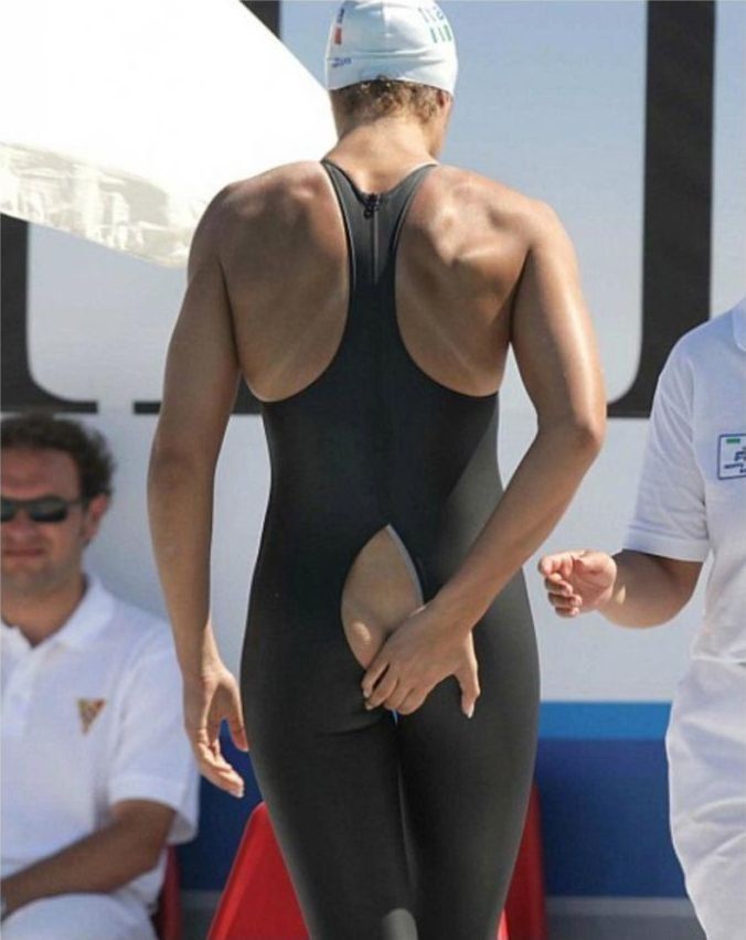 Мужчина в черном костюме для плавания на соревнованиях, вид сзади, часть ягодиц заметна.