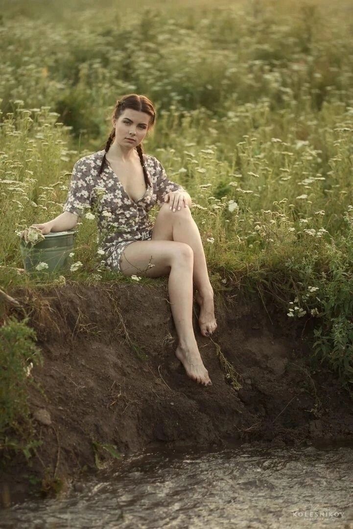 Женщина сидит на берегу у прилива/поля, босиком, в цветочном платье