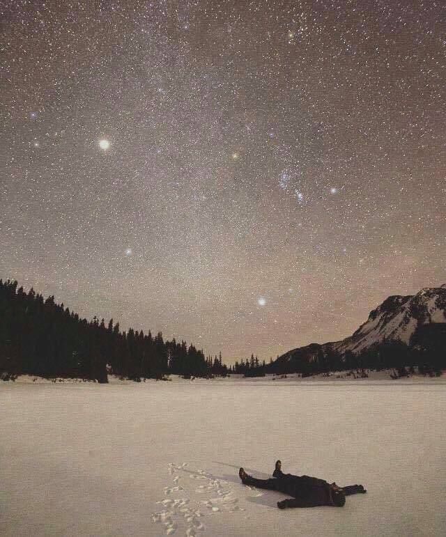 Зимний снег под звёздным небом, человек лежит на льду/снеге среди холмов и леса