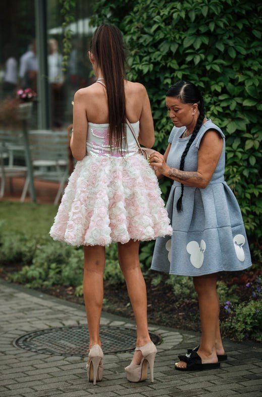 Две женщины на улице: молодая в пышном розовом платье, старшая поправляет её пояс