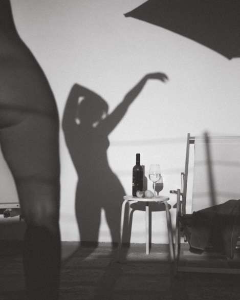 Черно-белая сценa: тень женщины на стене, столик с бутылкой и бокалом возле кровати.