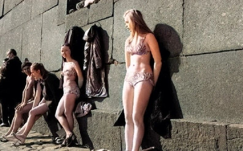 Несколько женщин в купальных костюмах позируют у каменной стены на улице