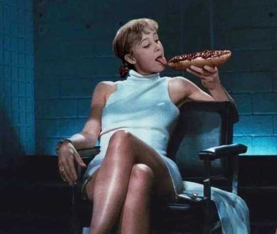 Женщина в светлом мини-платье сидит и облизывает пиццу