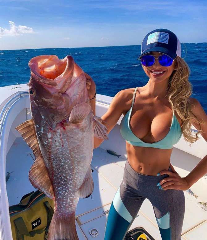 Женщина на лодке держит крупную рыбу над бортом океана.