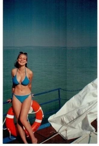 Женщина в синем купальнике стоит на палубе у моря, рядом спасательный круг.