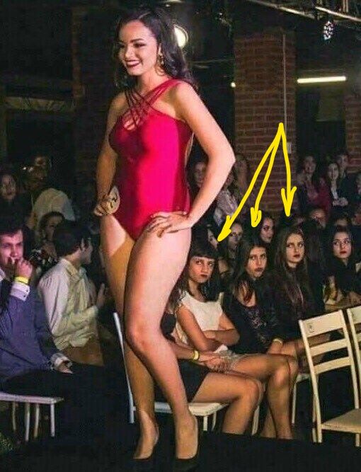 Женщина в красном боди на подиуме перед аудиторией во время показа мод