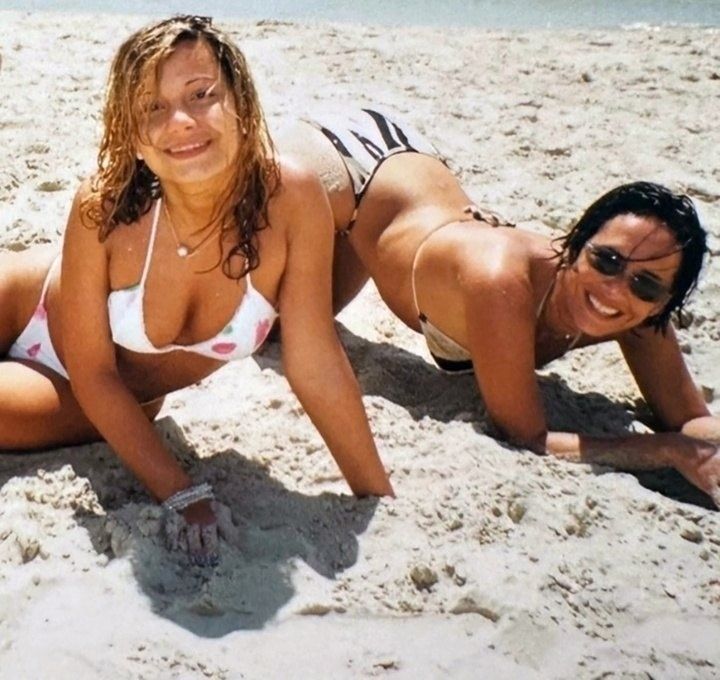 Две женщины в бикини на пляже копают песок и улыбаются.