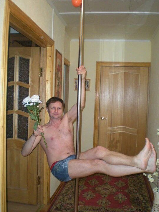 Мужчина держит букет и крутится на вертикальном шесте в коридоре дома.