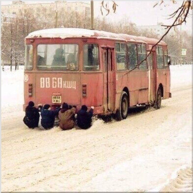 Сотрудники толкают застрявший в снегу старый автобус зимой.