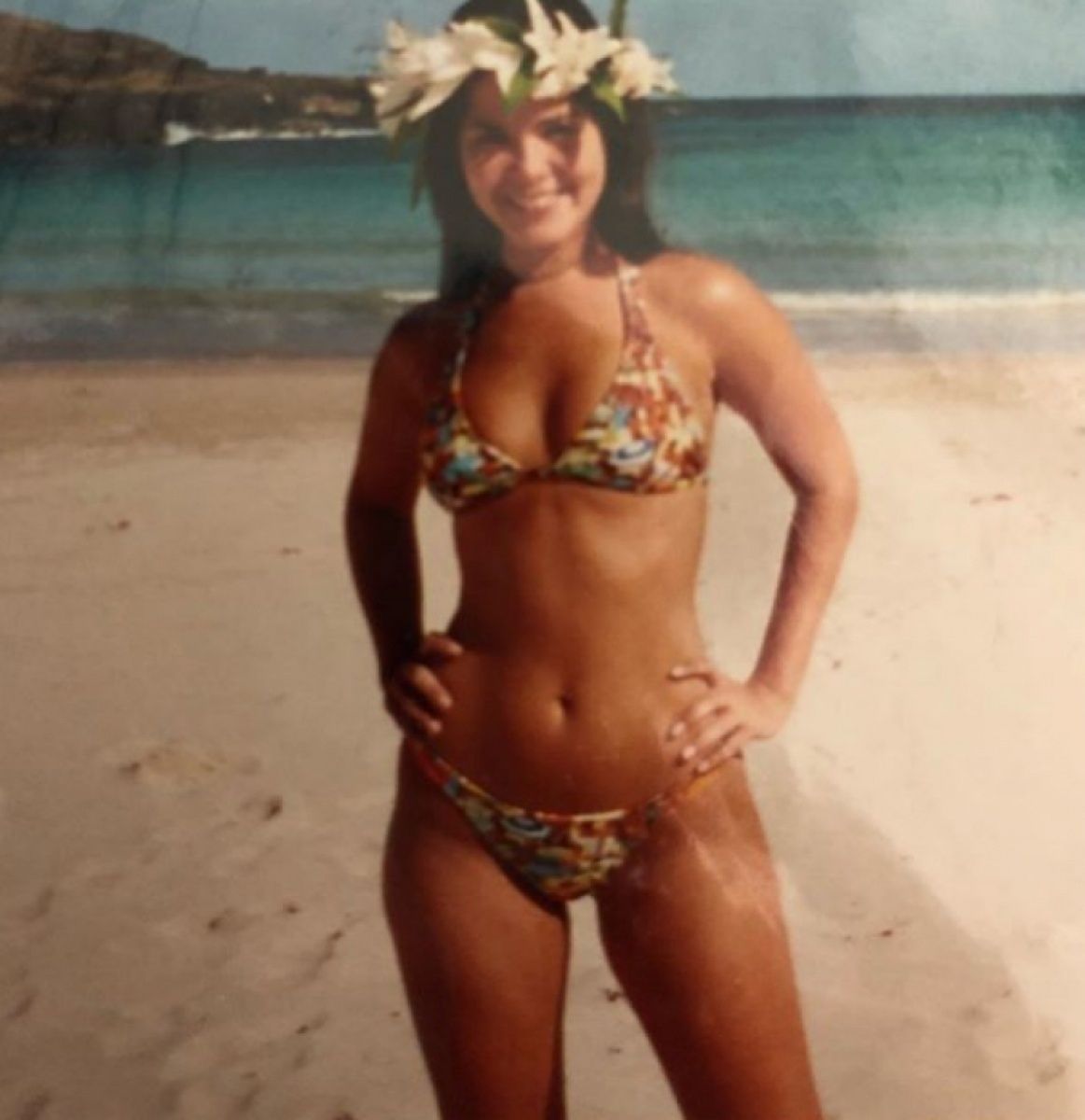 Женщина в цветном купальнике на пляже с венком из цветов.