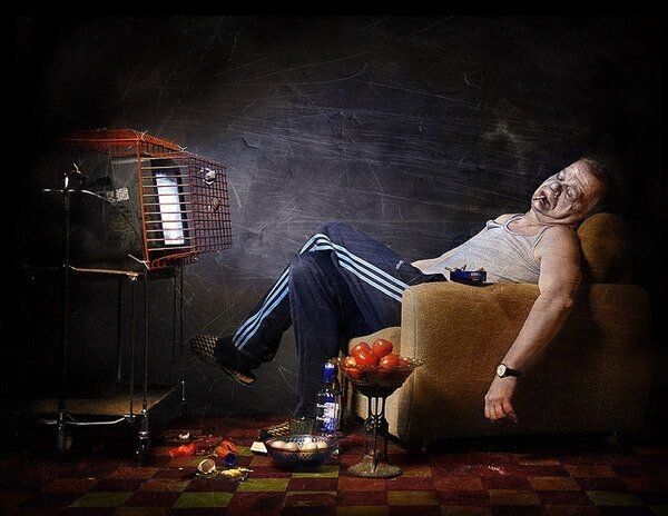 Пьяный мужчина сидит в кресле в темной комнате рядом с телевизором и столиком с едой