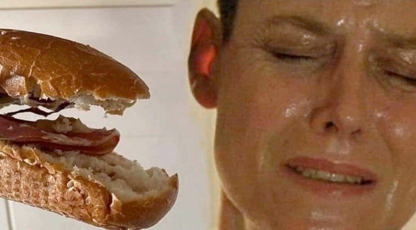 Мужчина с безудержным выражением лица рядом с половинкой большого сэндвича