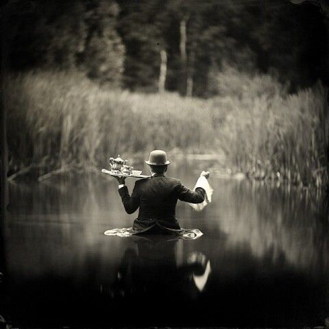 Человек в костюме в воде держит поднос и флаг в окружении камышей