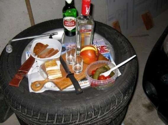 Неупорядоченный стол на шине: закуски, бутылки алкоголя, фрукты и посуда.