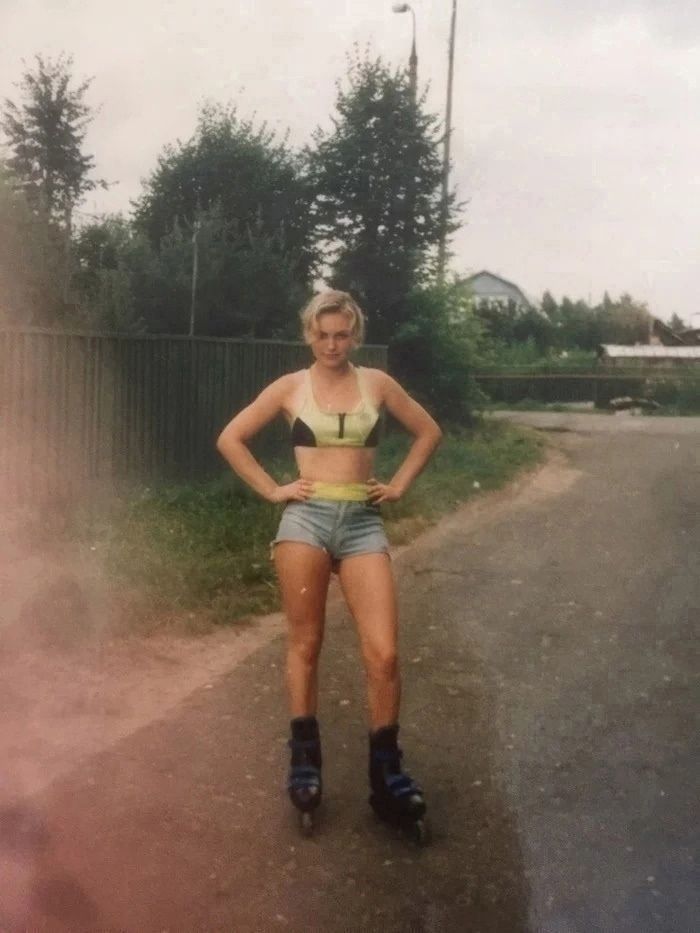 Женщина на роликах в открытом топе и шортах на проселочной улице.