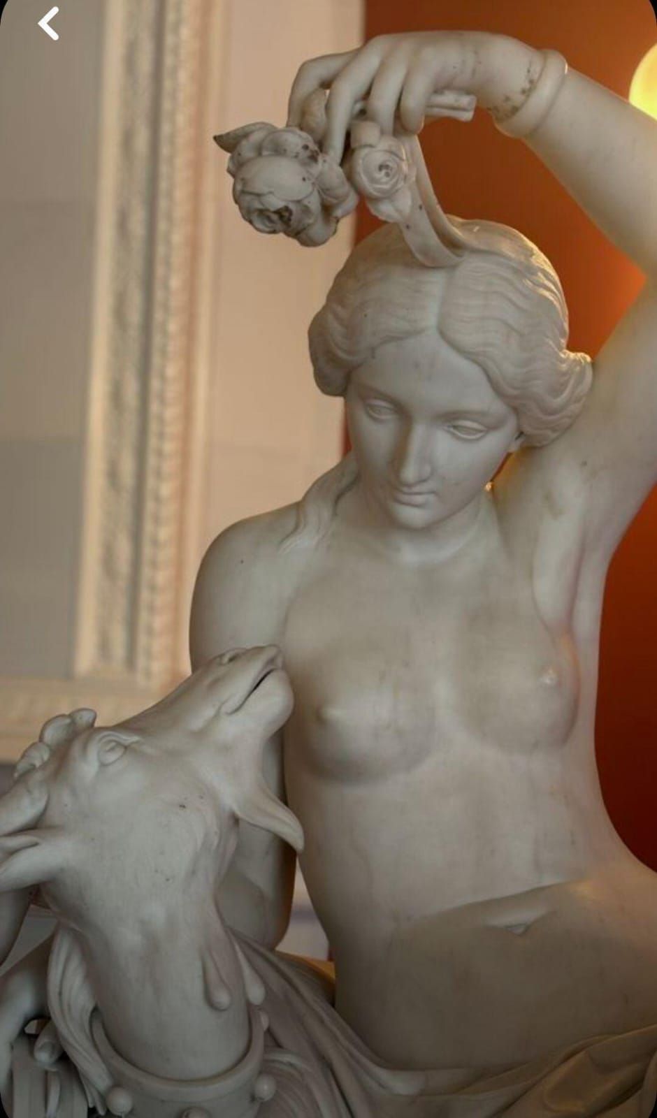 Мраморная статуя женщины в классической манере, рядом находится изображение животного (видна голова животного).