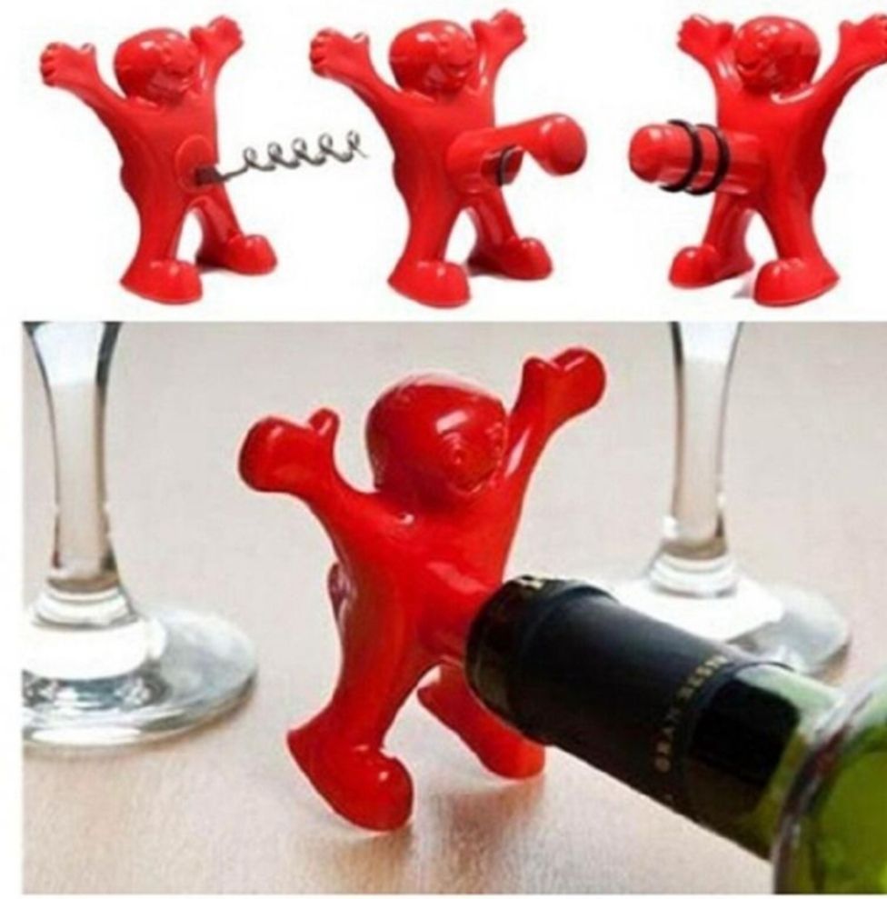 Три красные фигурки-игрушки и одна из них размахивает, рядом стоит бутылка шампанского.