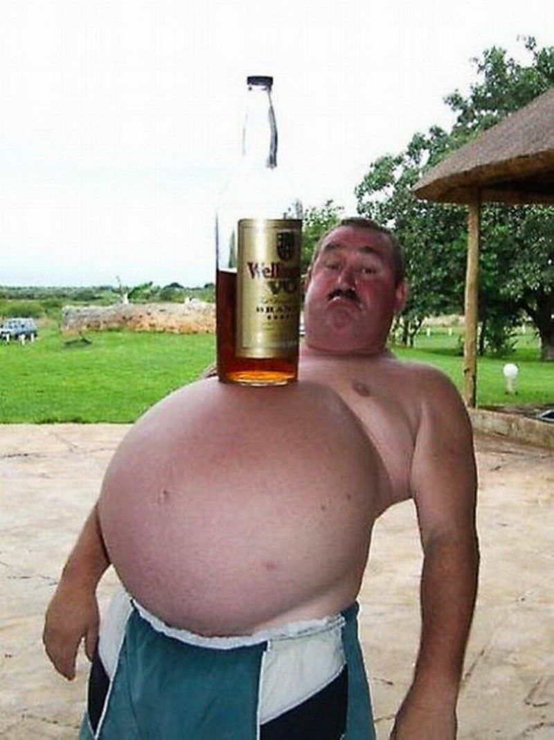 Толстый мужчина на улице держит бутылку виски на груди, улыбается.