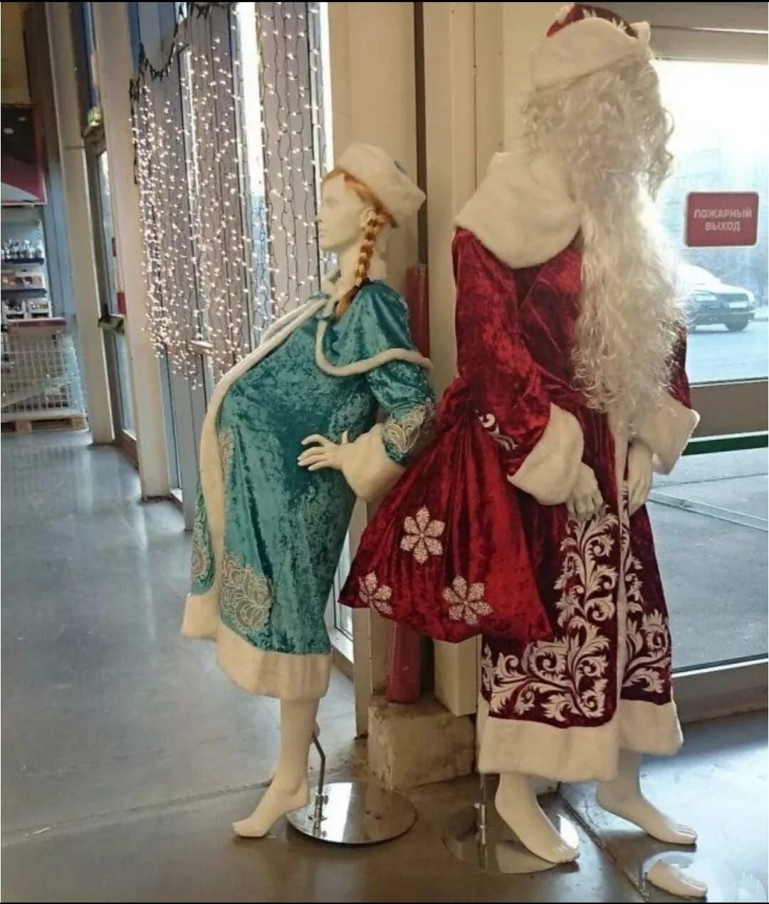 Две манекены в ярких нарядах Санта и снегурочки возле витрины магазина