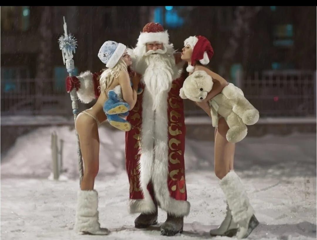 Санта в центре рядом с двумя женщинами в откровенных нарядах на снегу