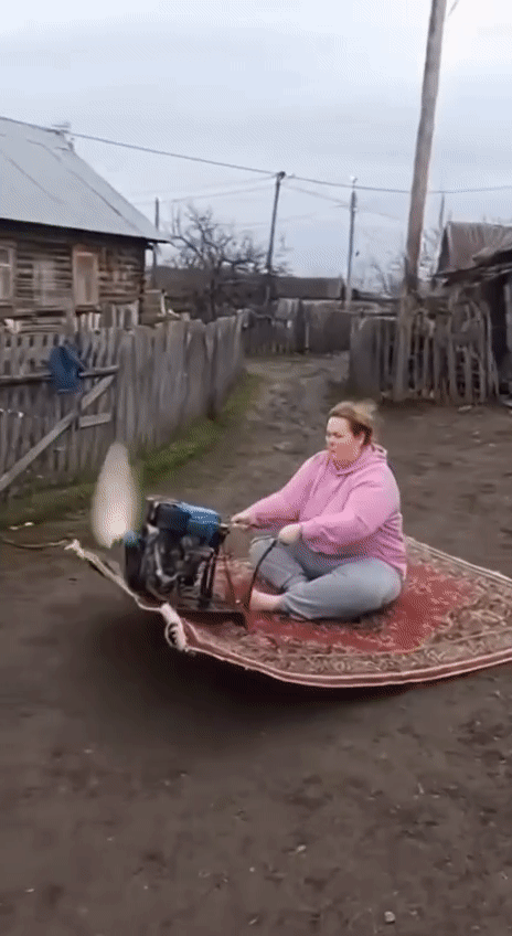 женщина на ковре с мотором едет по сельской улице
