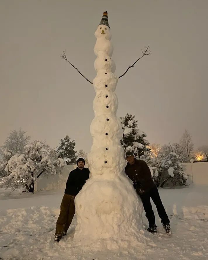 Двое мужчин возле гигантского снежного снеговика на зимнем участке парка.